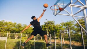 Cool black man playing basketball at sunrise, jumping high with energetic motion, representing esports lifestyle and the etsiosapp version from etruesports gaming performance tracking experience.
