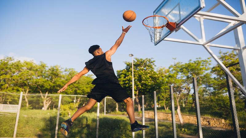Cool black man playing basketball at sunrise, jumping high with energetic motion, representing esports lifestyle and the etsiosapp version from etruesports gaming performance tracking experience.